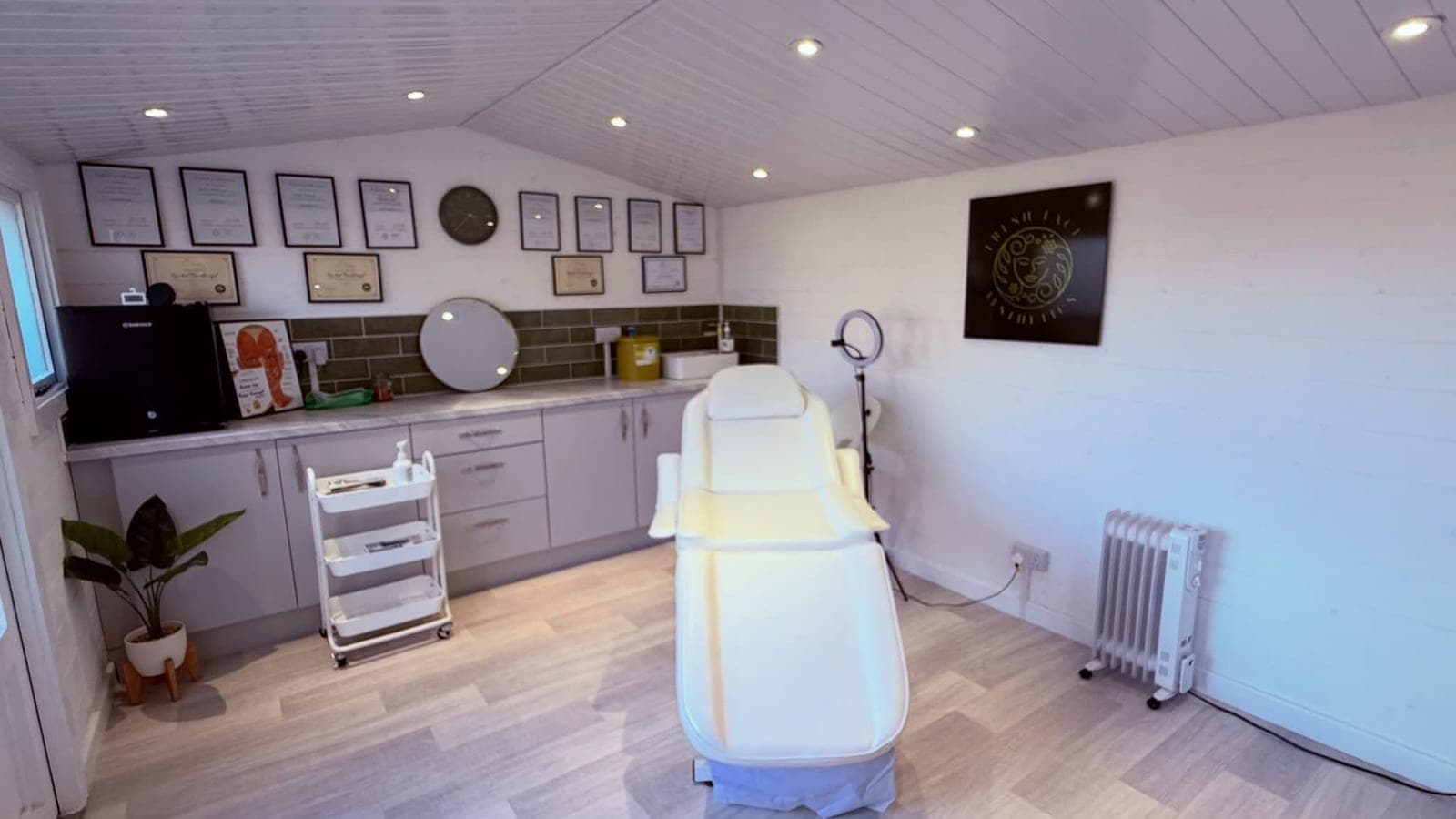 Rachel's treatment room: a white treatment chair, sage green tiles, grey cabinets and her certificates on the wall